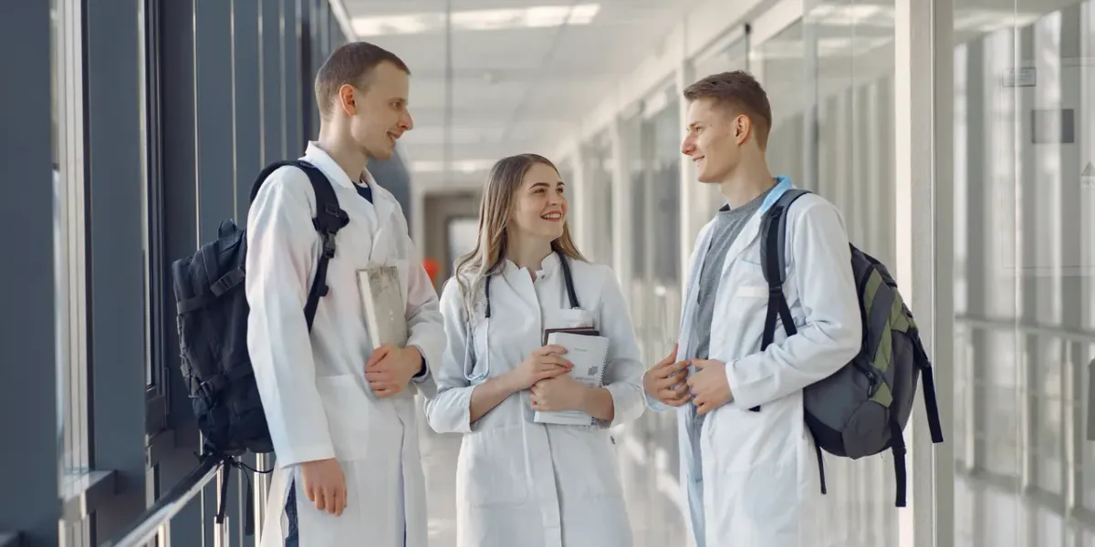 Troje młodych lekarzy w fartuchach rozmawia na korytarzu uczelni