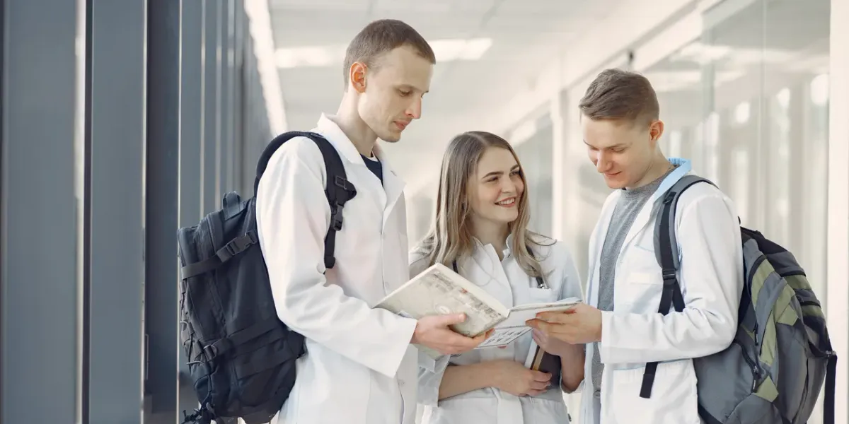 Troje młodych studentów medycyny w fartuchach rozmawia na korytarzu uczelni