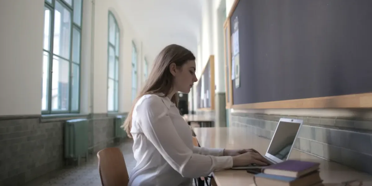 Studentka przy laptopie w korytarzu szkolnym — sprawdzanie wyników rekrutacji