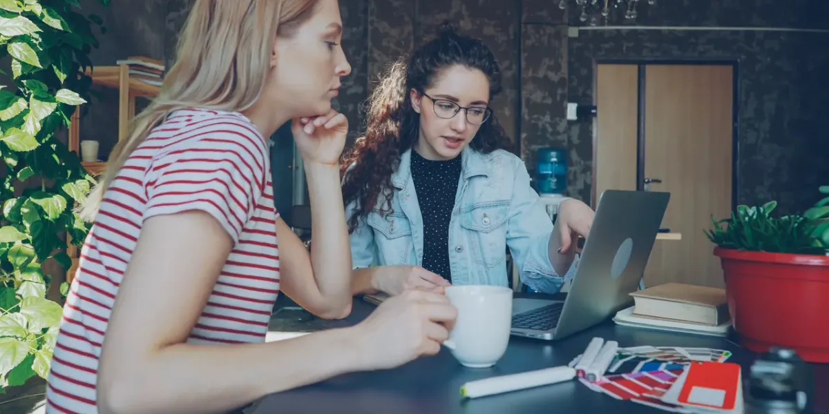 Dwie młode kobiety analizują dane na laptopie przy stole