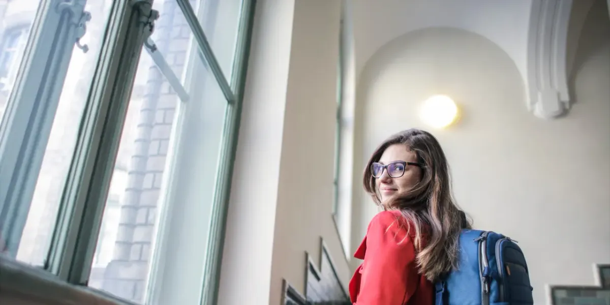 Studentka z plecakiem stojąca przy oknie w budynku uczelni