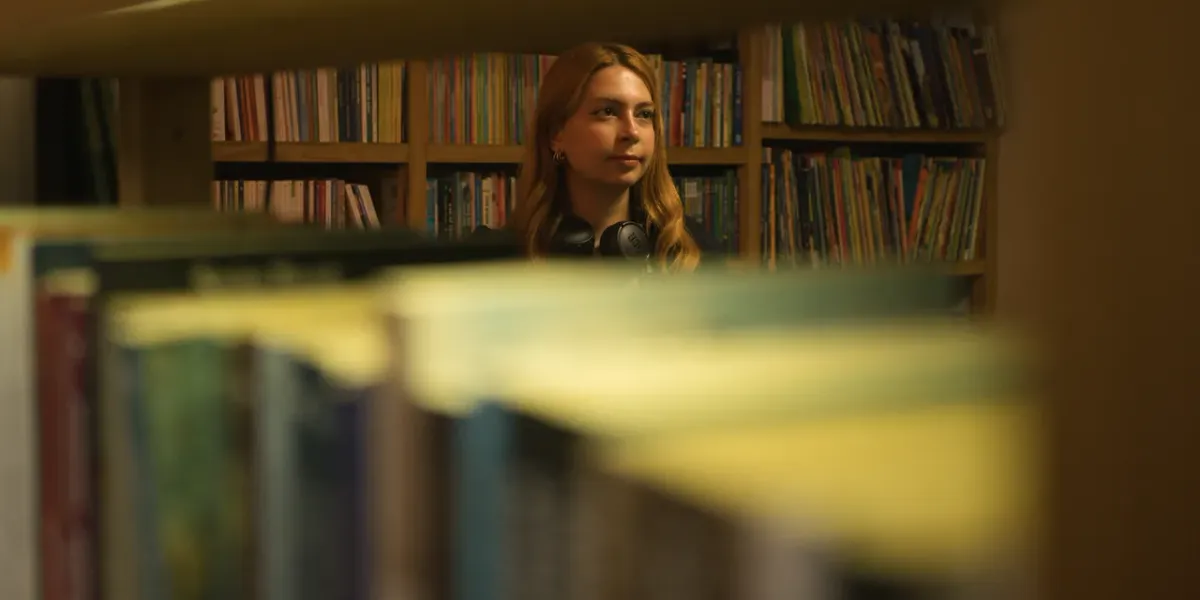 Młoda kobieta przeglądająca półki biblioteczne przez regał z książkami