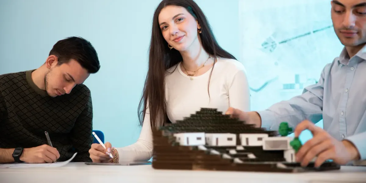Troje studentów pracujących nad makietą architektoniczną przy stole