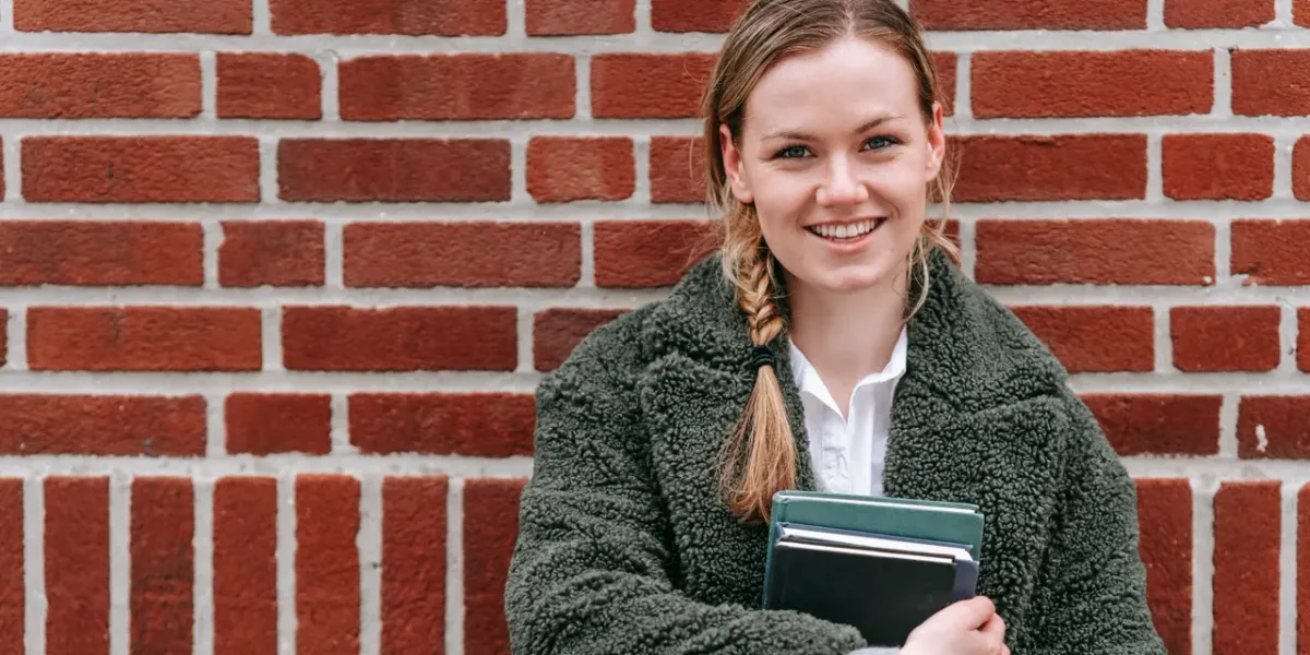 Młoda studentka z książkami przed budynkiem uczelni