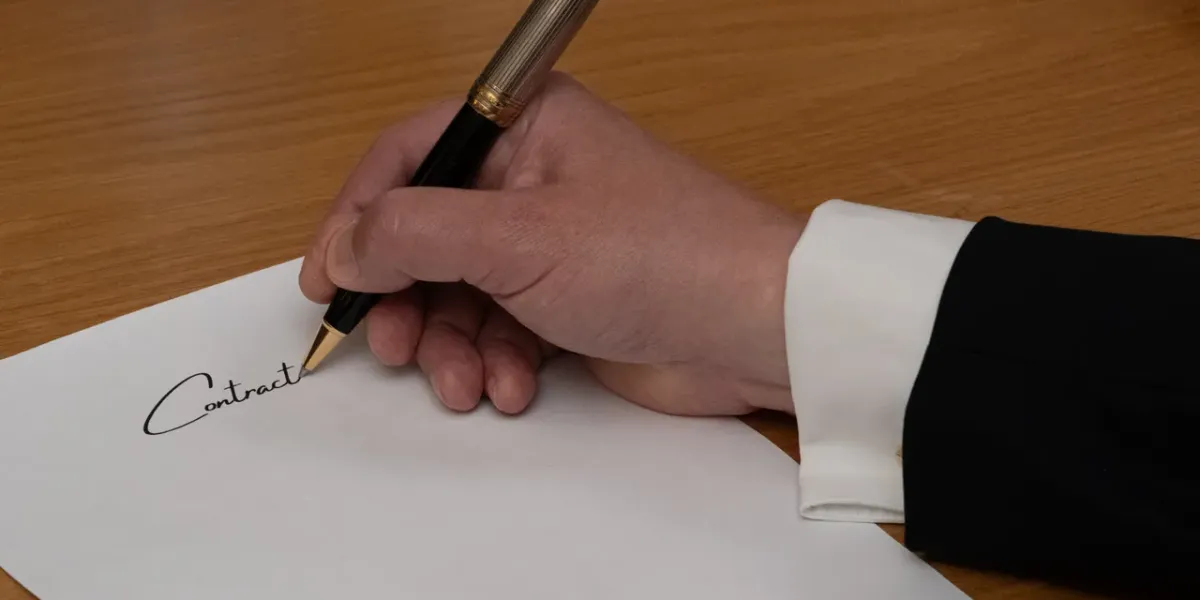 Dłoń podpisująca eleganckim piórem dokument z napisem Contract