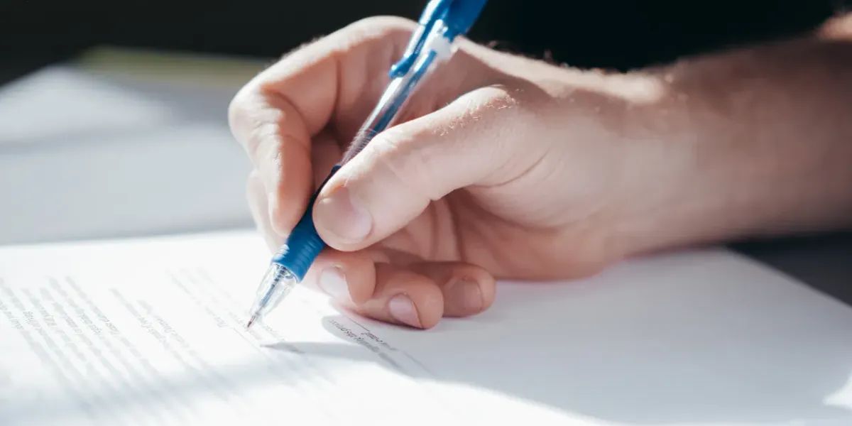 Dłoń podpisująca długopisem dokument na biurku