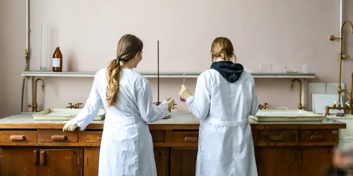 Dwie studentki w fartuchach laboratoryjnych przy stole laboratoryjnym