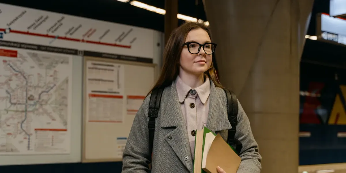 Młoda kobieta studentka z okularami i książkami na tle mapy metra